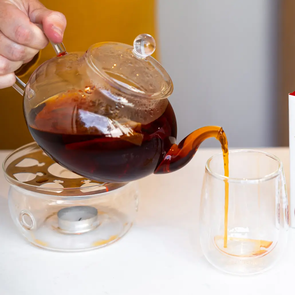 Rich caramel-coloured Carmién Tea being poured from a glass teapot into a clear glass, highlighting the authentic South African herbal tea experience and natural ingredients, perfect for health-conscious tea lovers.