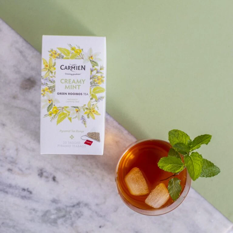 CarmiƩn Creamy Mint Rooibos Tea box with a glass of brewed tea garnished with mint leaves, ideal for tea lovers seeking refreshing rooibos blends.