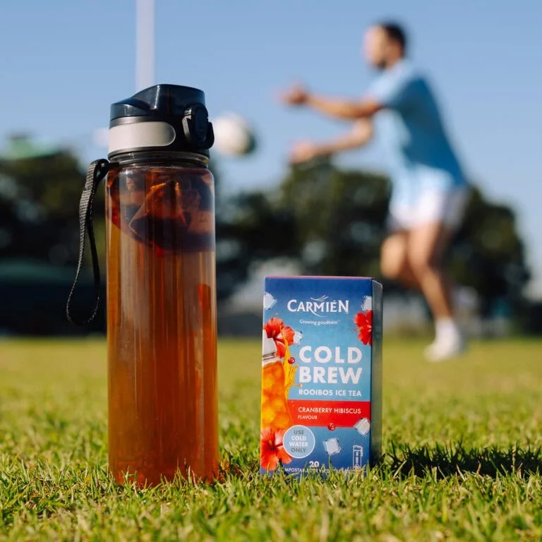 Carmién Cranberry Hibiscus Cold Brew Rooibos Tea in a box with a water bottle in the background, ideal for refreshing e-commerce sales.