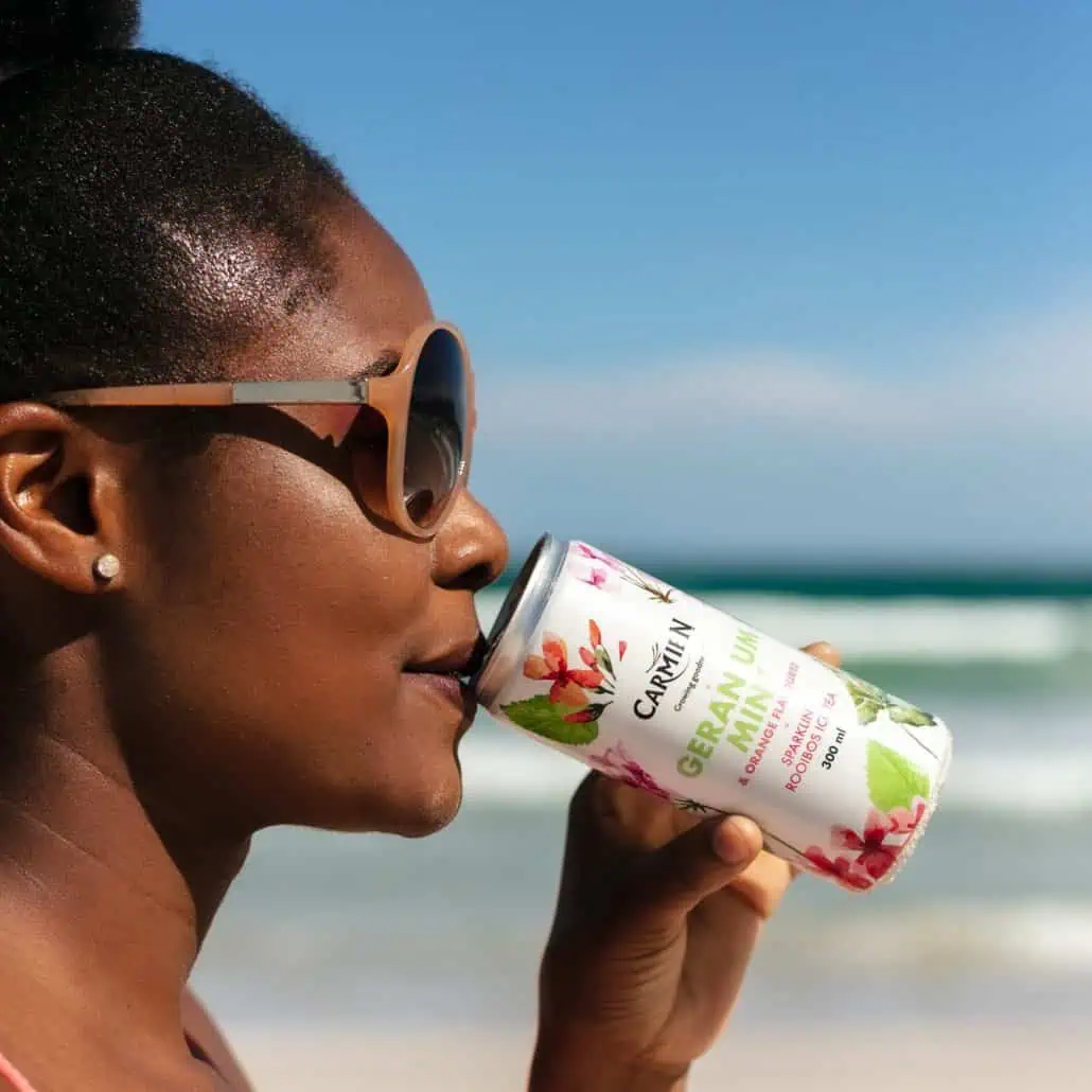 Refreshing woman enjoying Carmién Tea herbal drink on the beach, showcasing natural wellness and South African heritage, perfect for health-conscious consumers seeking organic tea beverages.