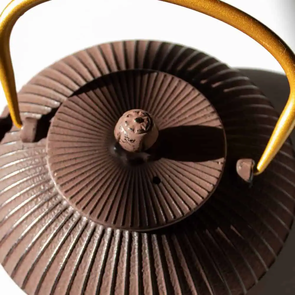 Elegant maroon and gold cast iron teapot with textured surface and sturdy handle, perfect for brewing and serving premium Carmién Tea.