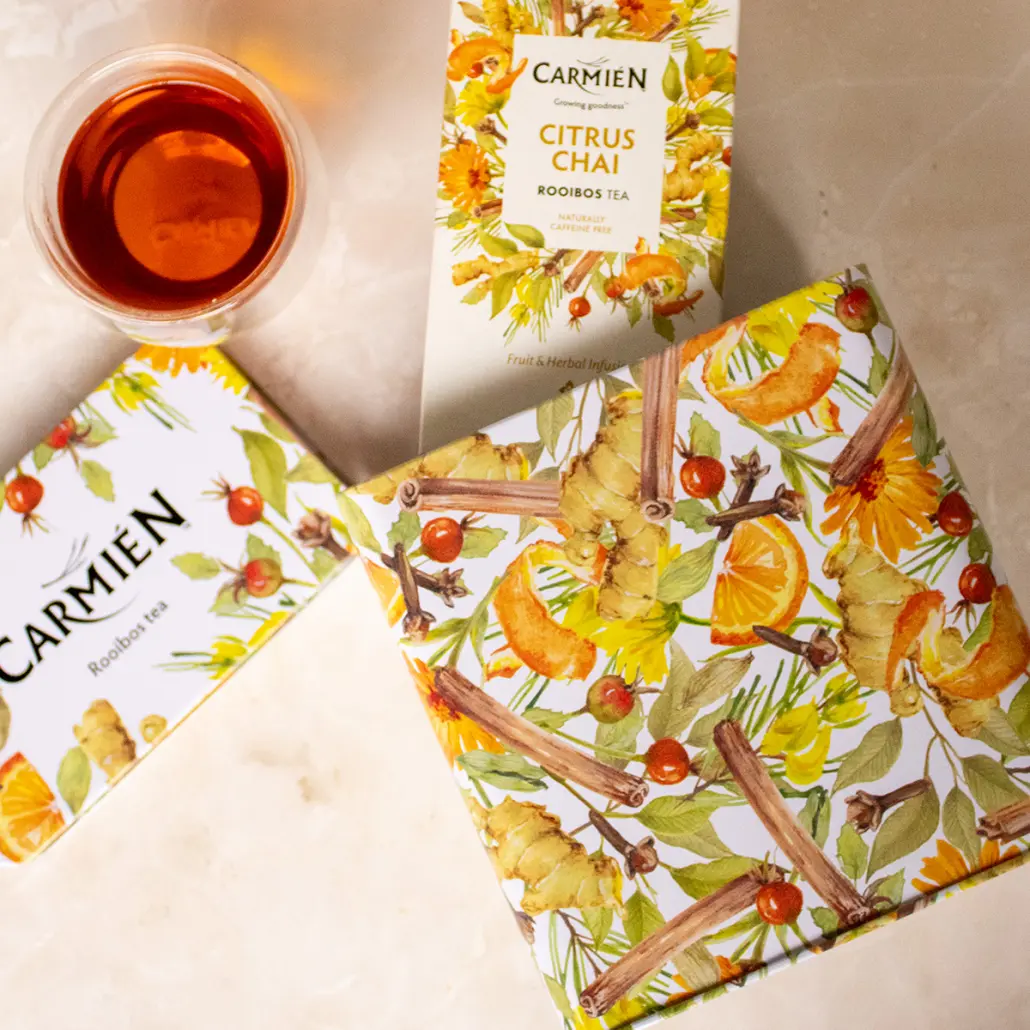 Orange and red citrus chai rooibos tea in a clear glass with a colourful tea box and packaging featuring citrus and ginger illustrations.