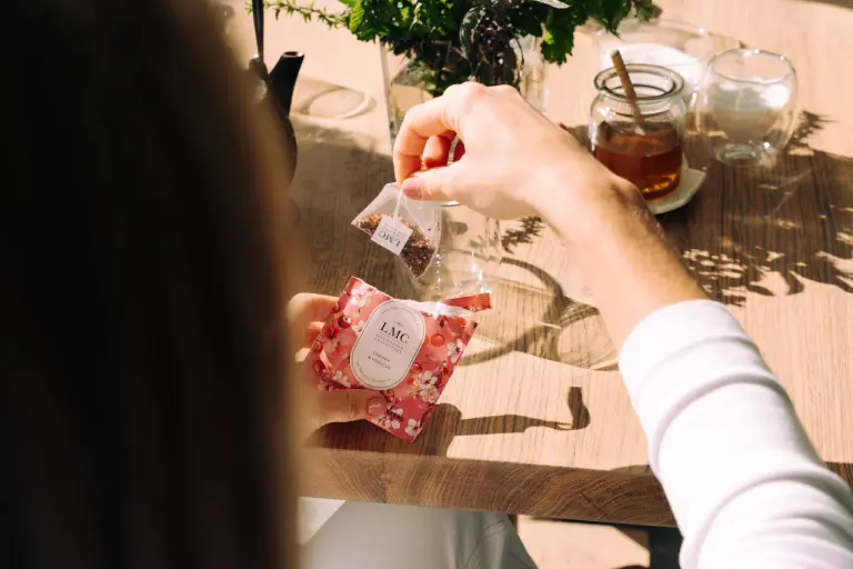 Aromatic CarmiƩn Tea being prepared with a tea bag on a wooden table, showcasing organic herbal tea leaves, perfect for wellness and relaxation.