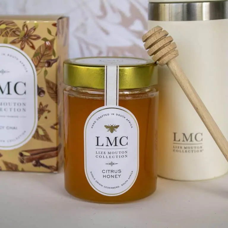 Rich, golden Citrus Honey in a glass jar with a gold lid, featuring a wooden honey dipper. Perfect for natural, South African high-quality honey and wellness products at CarmiƩn Tea.