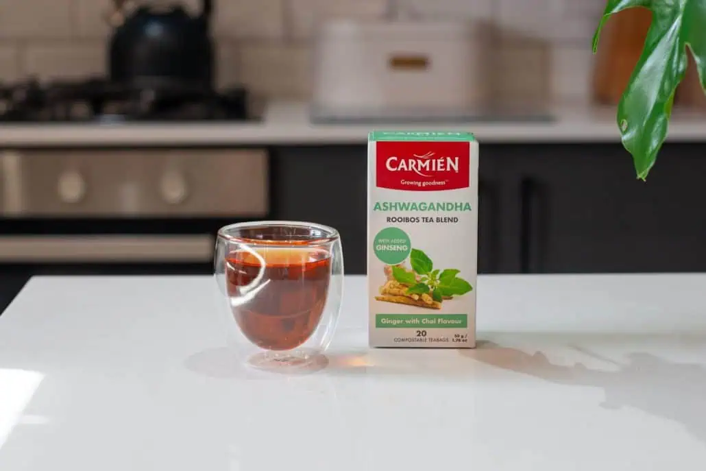 A glass of Carmién Ashwagandha herbal tea with the tea box on a kitchen counter, highlighting natural wellness and herbal benefits.
